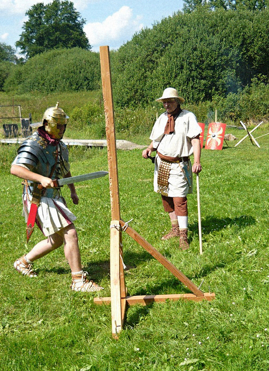 Legionář s mečem neboli gladiem. Velitel (centurio) mu na výcvikovém kůlu ukazuje vhodná místa pro útok na nepřítele.