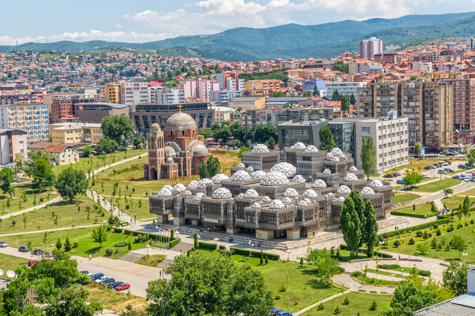 Metropole Priština s pozoruhodnou budovou Národní knihovny a nedokončenou a poničenou katedrálou Krista Spasitele.