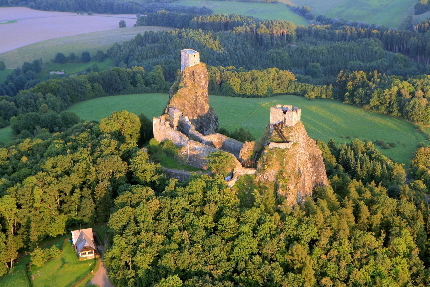 <h3>Hrad Trosky</h3><p>V Českém Ráji leží naše nejznámější zřícenina, symbolicky střežená dvěma čedičovými sopouchy <strong>Pannou</strong> a <strong>Babou</strong>. Řada badatelů už více než dvě stě let prozkoumává tajné chodby a jeskyně pod <strong>Troskami</strong>. Někteří tvrdí, že se tu dokonce ukrývá obrovský poklad. Nikdo ho ale zatím neobjevil. Můžete to zkusit vy, třeba budete mít štěstí. Zatím ale každému zabránily balvany, vzpříčené v průchodu do rozvětvených chodeb pod hradem. A také varovné nápisy staré mnoho století. Smrt hrozí těm, kteří svou zvědavost neudrží na uzdě!</p><p>Když ale odoláte a nebudete rušit ukrytá tajemství, odmění vás nádherný výhled po krajině. A nemusíte ani stoupat přímo na hrad. V okolí je mnoho turistických tras, skalních útvarů a romantických tůněk. <em>(foto: Wikimedia Commons, Zdeněk Fiedler, </em><em>CC BY-SA 3.0)</em></p>